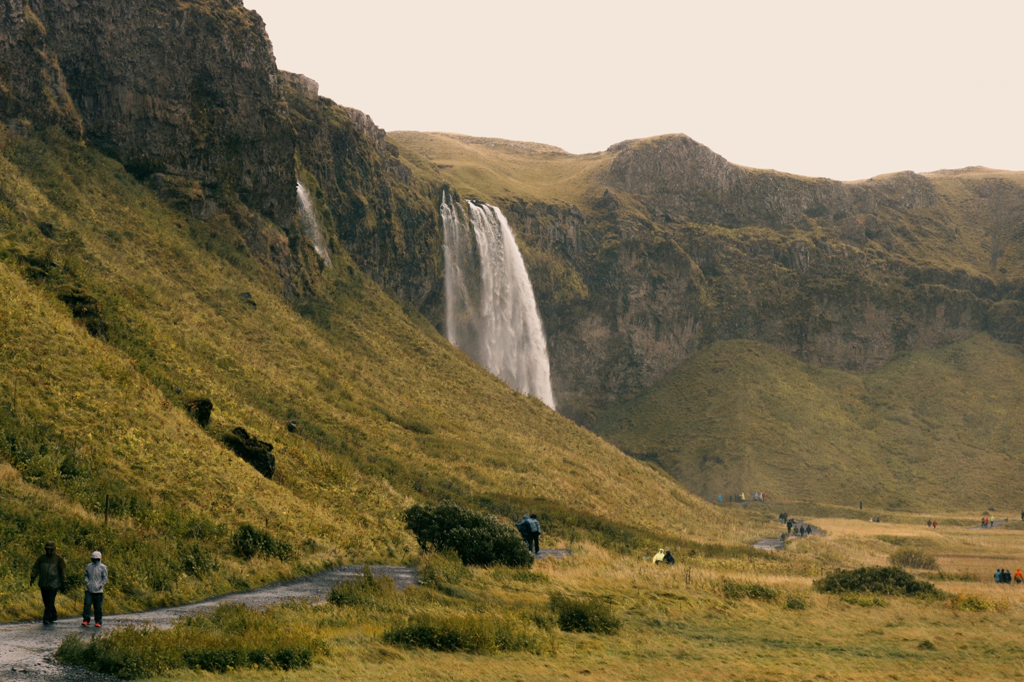 A waterfall over a green hillside, with people walking in the distance