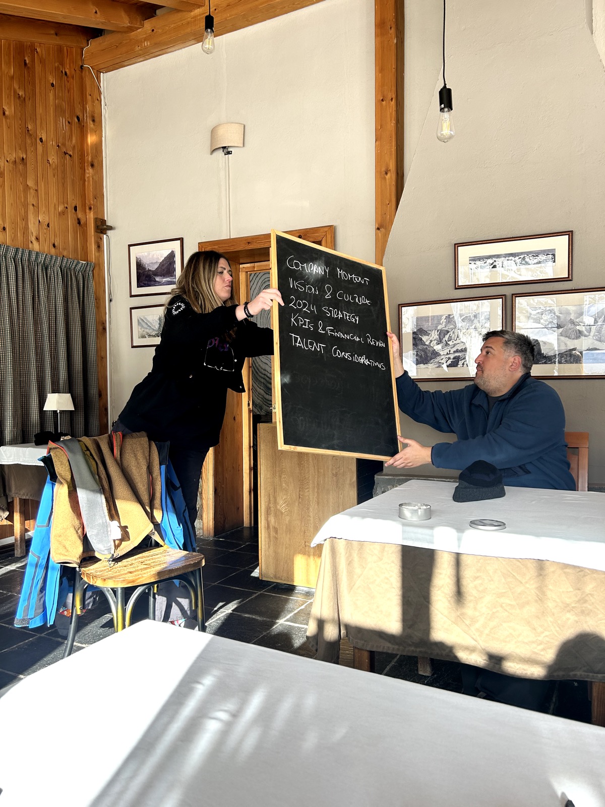 Two people holding a chalkboard in a wood-panelled room