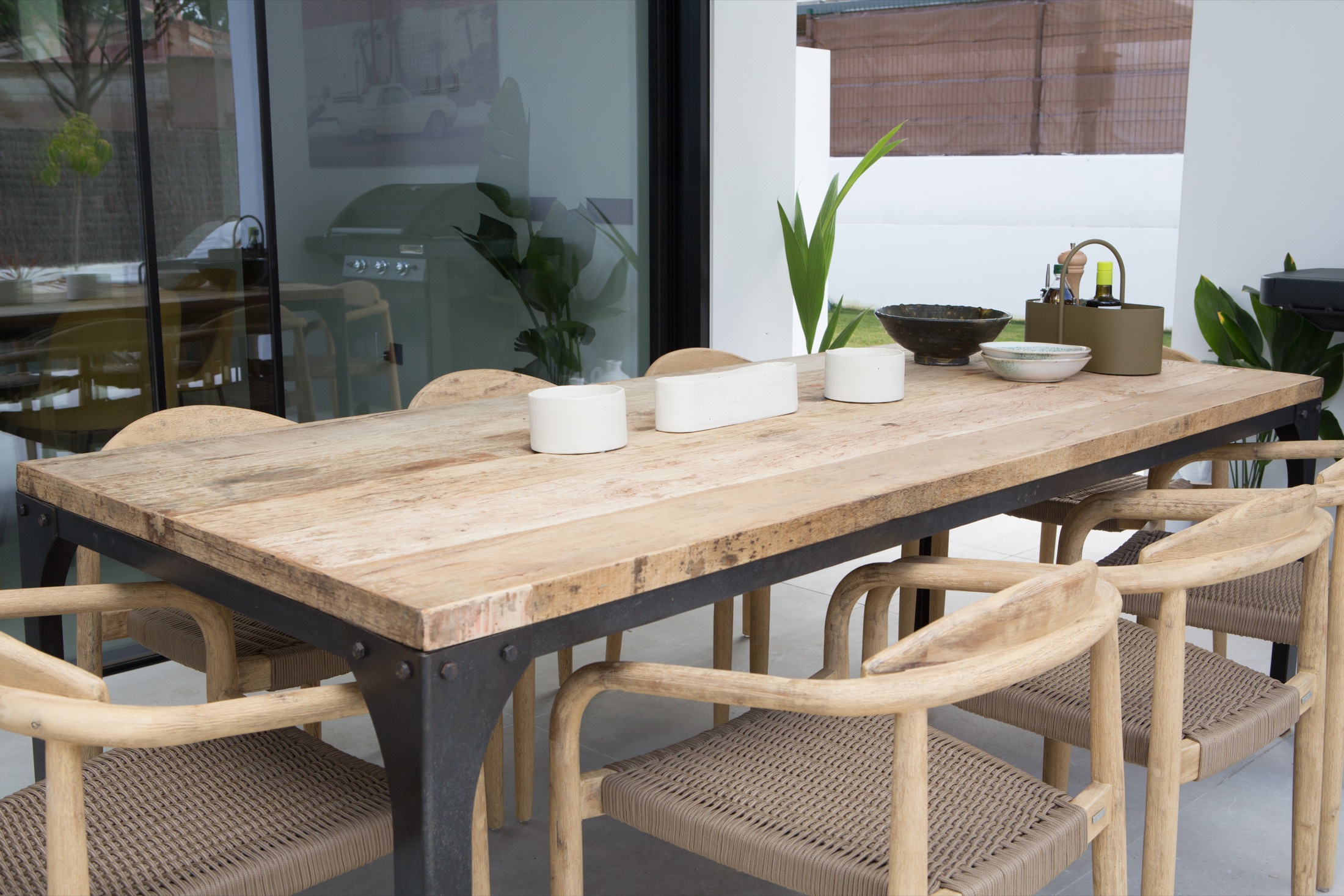 A long wooden table with woven chairs on a covered terrace